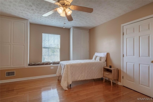 bedroom with visible vents, light wood-style flooring, ceiling fan, a textured ceiling, and baseboards