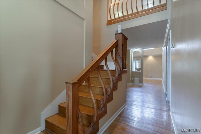 stairway with a high ceiling, baseboards, and wood finished floors