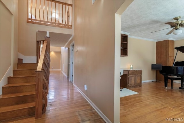 corridor with crown molding, a textured ceiling, wood finished floors, baseboards, and stairs