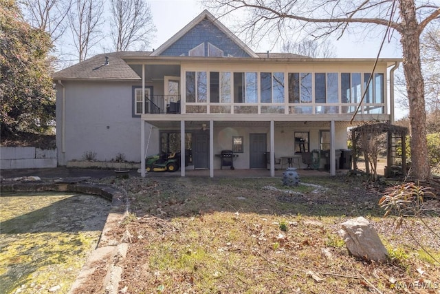 back of property with a patio area, a shingled roof, a sunroom, and stucco siding