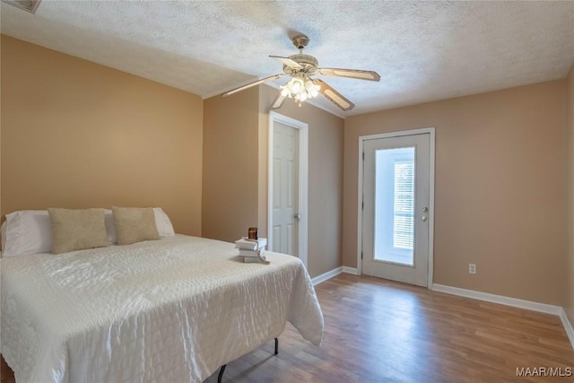 bedroom with a textured ceiling, ceiling fan, wood finished floors, baseboards, and access to outside