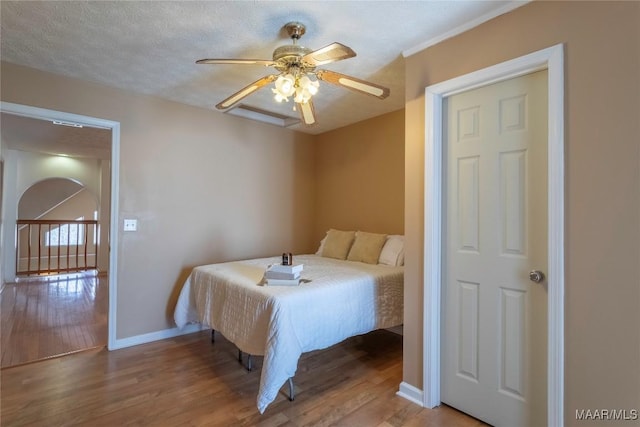 bedroom with a ceiling fan, a textured ceiling, baseboards, and wood finished floors