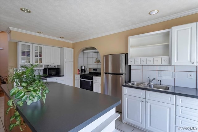 kitchen featuring arched walkways, stainless steel appliances, a sink, open shelves, and dark countertops