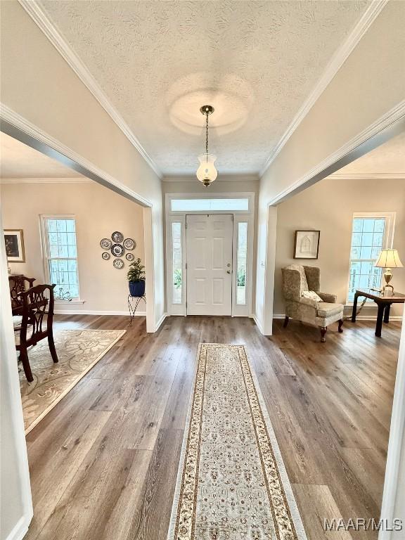 foyer entrance featuring a textured ceiling, wood finished floors, a wealth of natural light, and crown molding