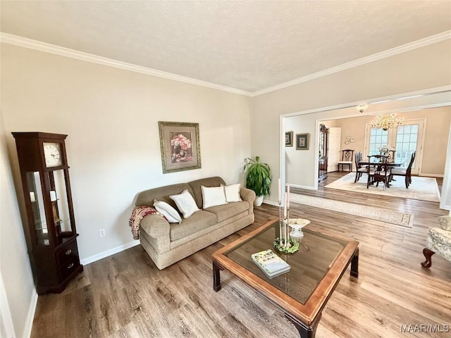 living room featuring a chandelier, crown molding, baseboards, and wood finished floors