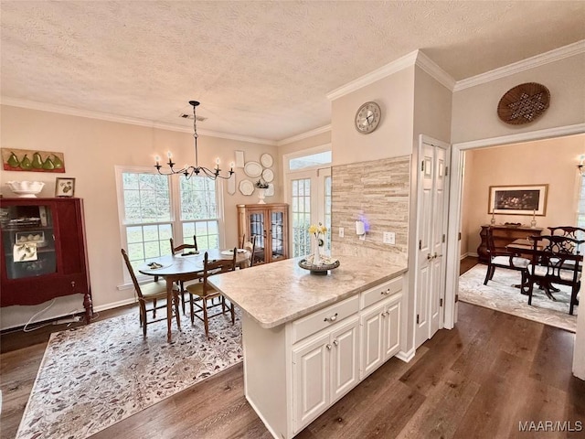 kitchen featuring dark wood-type flooring, white cabinets, crown molding, and an inviting chandelier