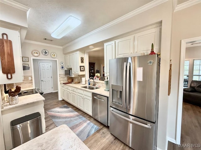 kitchen featuring appliances with stainless steel finishes, white cabinetry, a sink, and wood finished floors