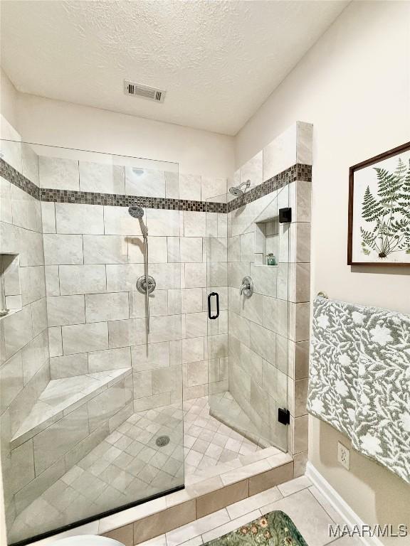 bathroom with visible vents, a shower stall, and a textured ceiling