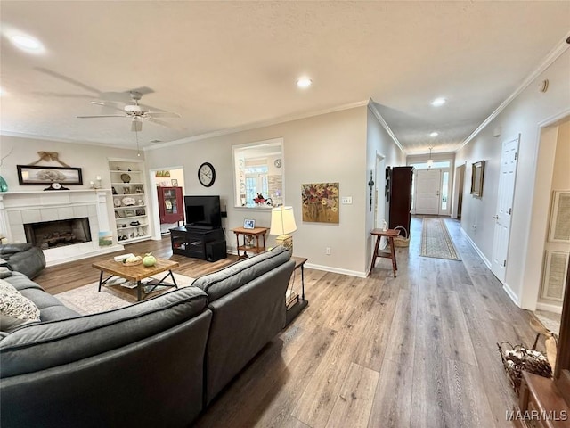 living room with built in shelves, baseboards, ornamental molding, light wood-type flooring, and a tiled fireplace