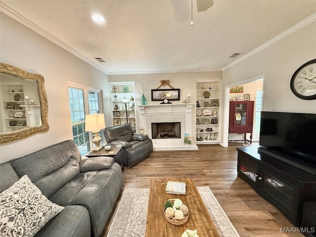 living room featuring built in features, crown molding, a textured ceiling, wood finished floors, and a tile fireplace