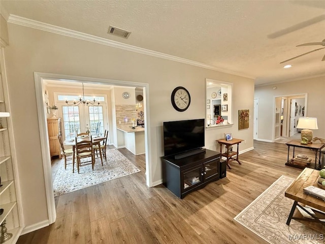 living area with a textured ceiling, ornamental molding, ceiling fan with notable chandelier, and wood finished floors