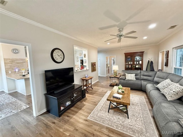 living room with ornamental molding, visible vents, baseboards, and wood finished floors