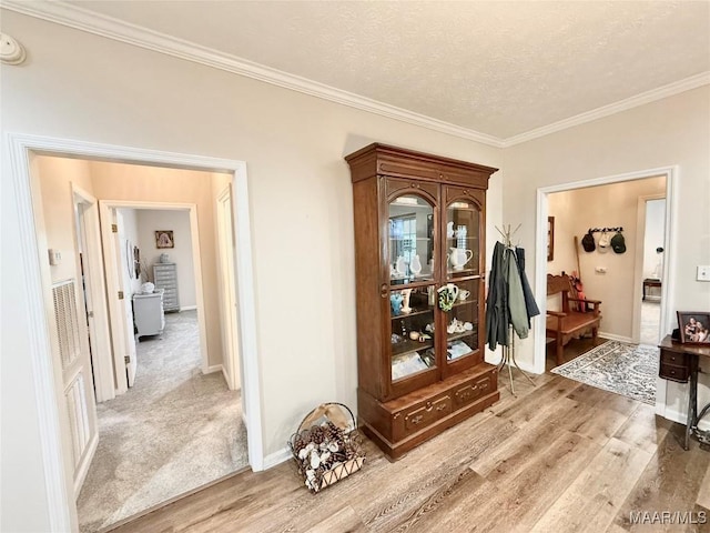 foyer with light wood-style floors, baseboards, ornamental molding, and a textured ceiling