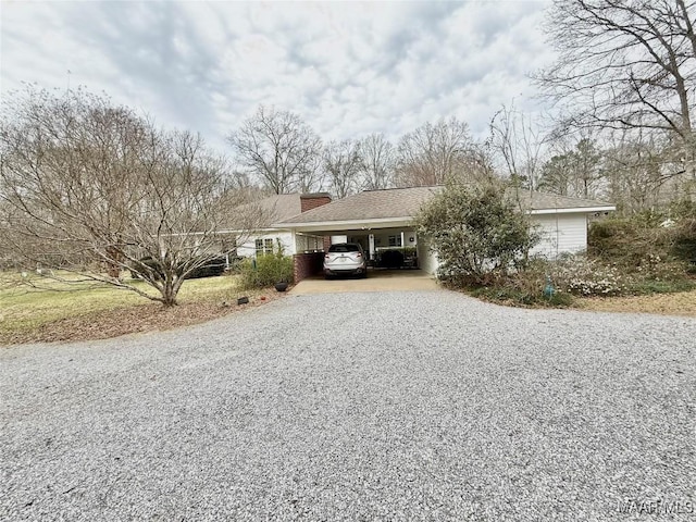 view of front of house with driveway, an attached carport, a chimney, and a shingled roof