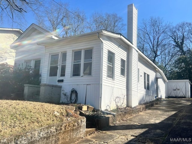 view of home's exterior with concrete driveway, an outdoor structure, and a chimney