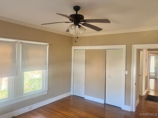 unfurnished bedroom featuring dark wood-type flooring, a ceiling fan, baseboards, a closet, and crown molding