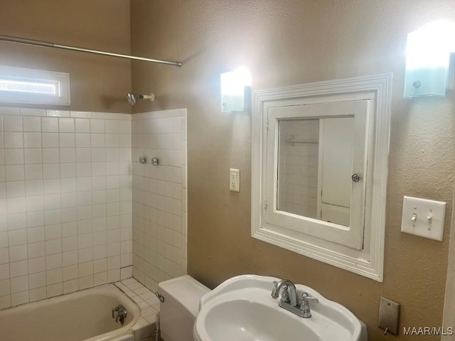 bathroom featuring shower / washtub combination, a textured wall, a sink, and toilet