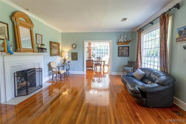 living area featuring a fireplace with flush hearth, ornamental molding, baseboards, and wood finished floors