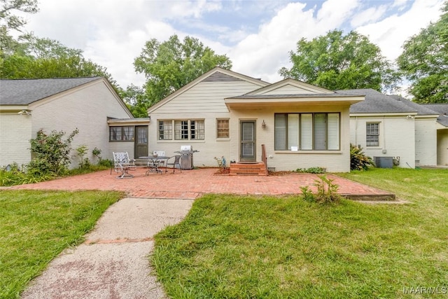 rear view of property featuring a yard, brick siding, cooling unit, and a patio