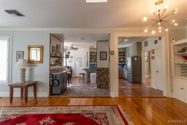 foyer entrance featuring baseboards, visible vents, ornamental molding, wood finished floors, and ceiling fan with notable chandelier