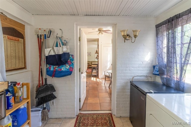 clothes washing area featuring light tile patterned floors, laundry area, brick wall, a ceiling fan, and independent washer and dryer