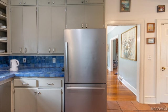 kitchen with tile counters, gray cabinets, freestanding refrigerator, and decorative backsplash