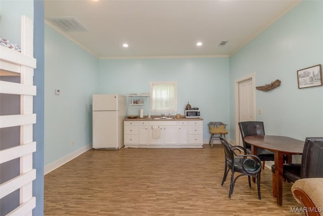 kitchen with freestanding refrigerator, white cabinets, visible vents, and a sink