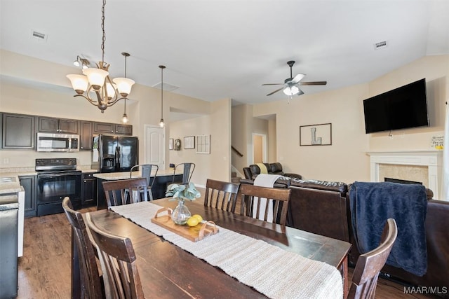 dining space featuring a fireplace, visible vents, wood finished floors, and ceiling fan with notable chandelier