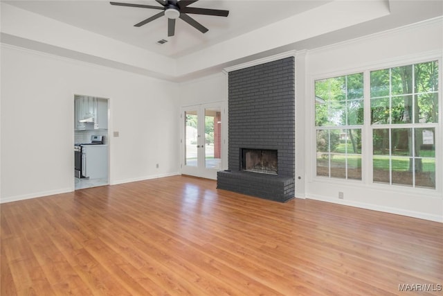 unfurnished living room with a tray ceiling, french doors, light wood-style flooring, a brick fireplace, and ceiling fan