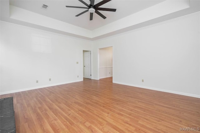 spare room featuring light wood-type flooring, a raised ceiling, a ceiling fan, and baseboards