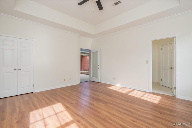 unfurnished bedroom with light wood-style flooring, visible vents, a raised ceiling, and baseboards