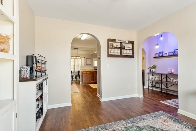 corridor featuring arched walkways, dark wood-type flooring, and baseboards