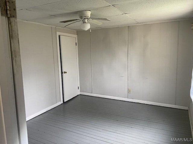 spare room with a paneled ceiling, wood-type flooring, a ceiling fan, and baseboards