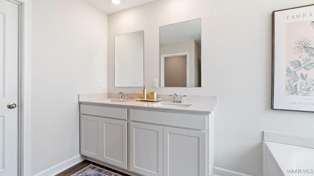 bathroom with double vanity, a sink, a bathtub, and baseboards