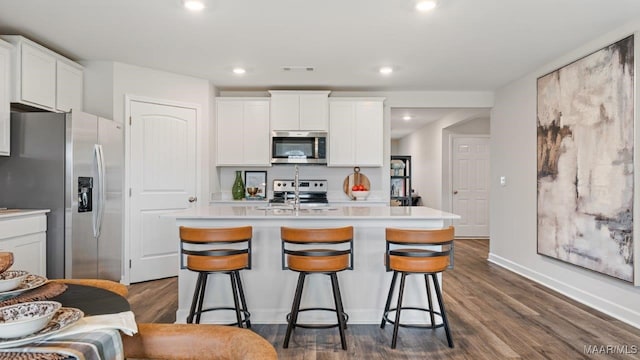 kitchen with light countertops, appliances with stainless steel finishes, dark wood-type flooring, a kitchen island with sink, and white cabinets