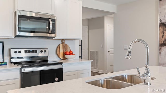 kitchen featuring stainless steel appliances, visible vents, white cabinets, a sink, and light stone countertops