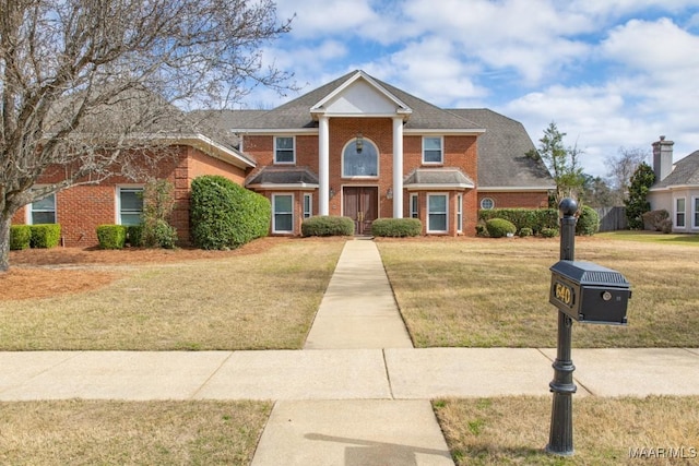 neoclassical home featuring brick siding and a front yard