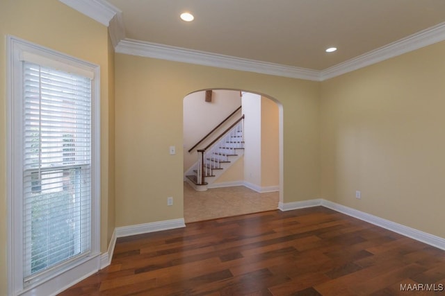 empty room with arched walkways, baseboards, wood finished floors, and crown molding