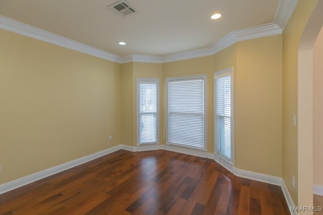 spare room with arched walkways, wood finished floors, visible vents, baseboards, and ornamental molding