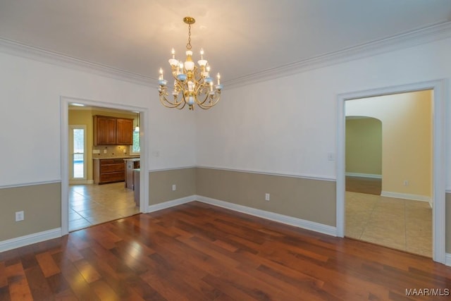 unfurnished room featuring arched walkways, a notable chandelier, crown molding, and wood finished floors