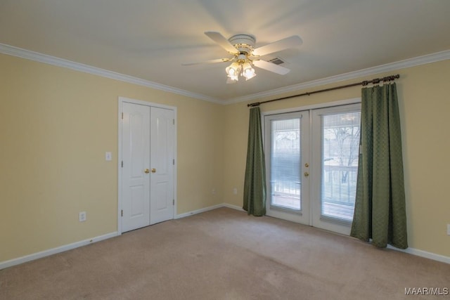 carpeted spare room featuring visible vents, baseboards, a ceiling fan, crown molding, and french doors