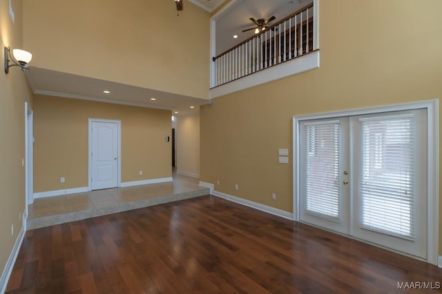 unfurnished room featuring crown molding, a towering ceiling, baseboards, and wood finished floors