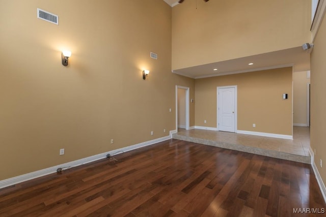 unfurnished room with dark wood-style floors, a towering ceiling, visible vents, and baseboards