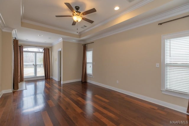 spare room with a tray ceiling, crown molding, dark wood-type flooring, a ceiling fan, and baseboards