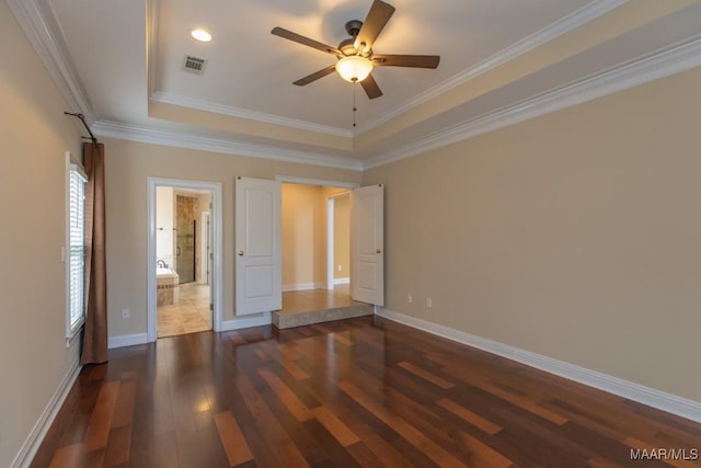 unfurnished bedroom with a tray ceiling, visible vents, baseboards, and wood finished floors