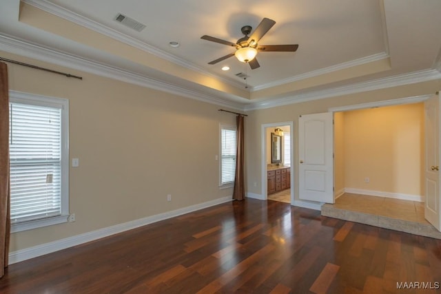 unfurnished room with a tray ceiling, visible vents, ornamental molding, wood finished floors, and baseboards