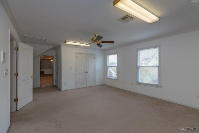 unfurnished bedroom featuring a closet, light colored carpet, visible vents, ornamental molding, and ceiling fan