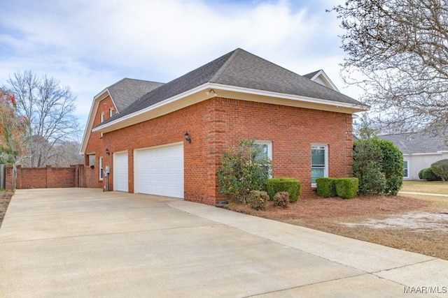 view of home's exterior featuring a shingled roof, fence, concrete driveway, and brick siding