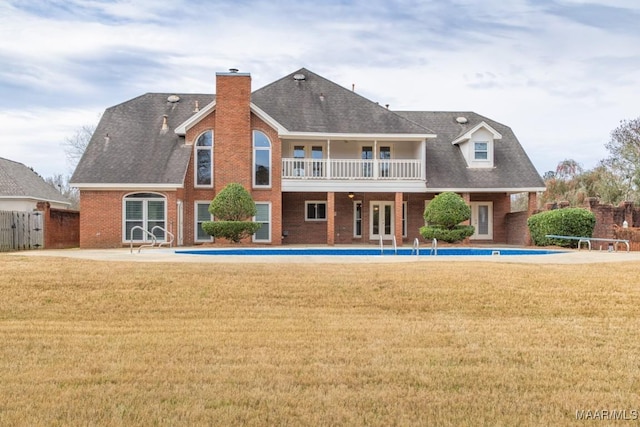 rear view of property featuring french doors, brick siding, a lawn, and a balcony