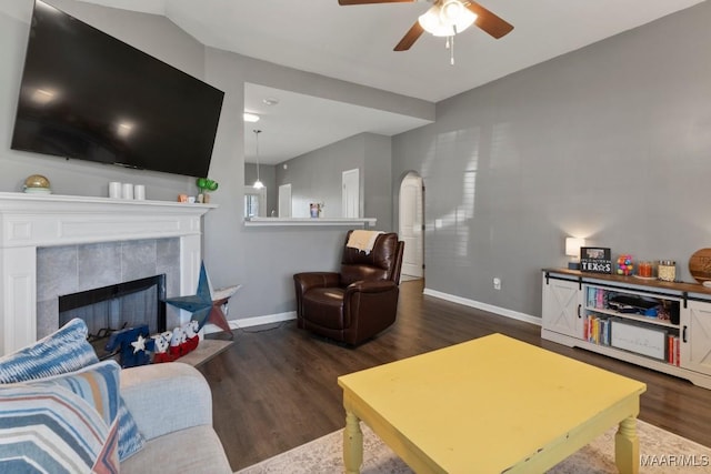 living room featuring dark wood-type flooring, a tile fireplace, arched walkways, and baseboards